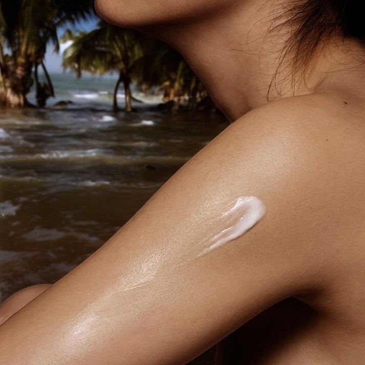 Body lotion on skin against a tropical beach background.